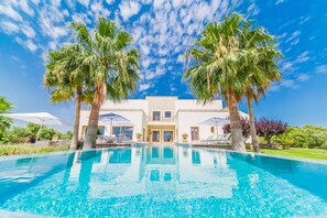 A modern villa with a swimming pool, palm trees, and a clear blue sky.