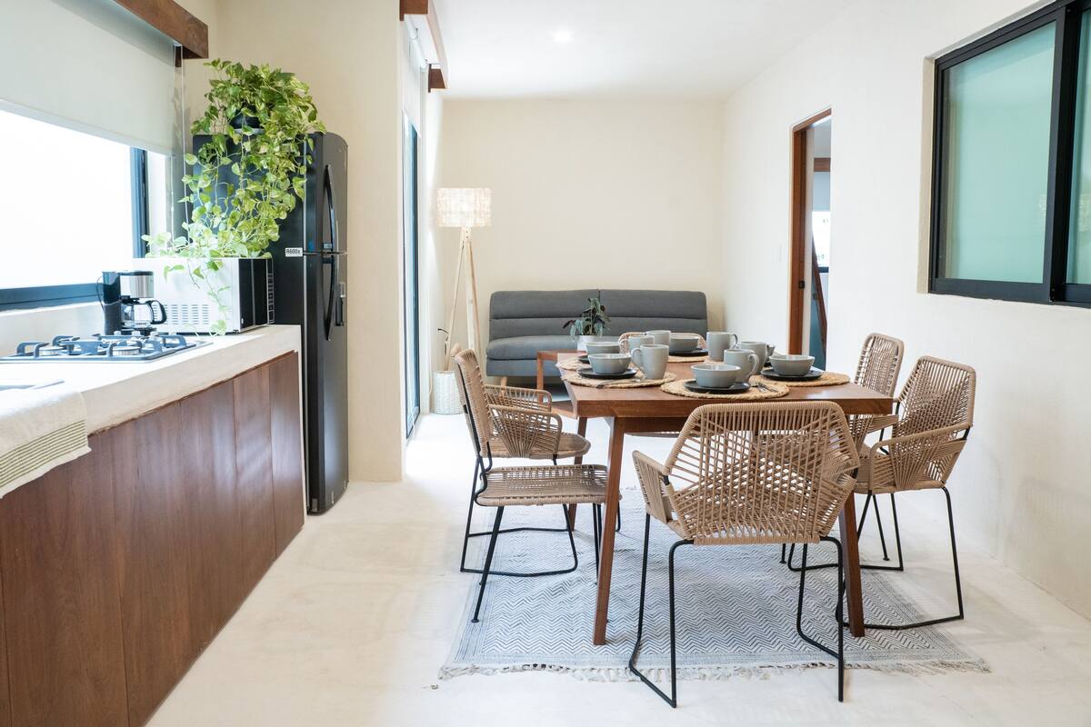 Une cuisine moderne avec un coin repas, comprenant un réfrigérateur encastré, une machine à café et une table à manger avec des chaises en osier.
