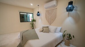 A bedroom with a bed, a window, an air conditioner, a macrame wall hanging, and a hanging light fixture. - Mayanah Condohotel Bacalar (Bacalar)