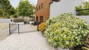Ett modernt hus med en träfasad och en grå vägg. En grusuppfart leder fram till en svart grind i metall.