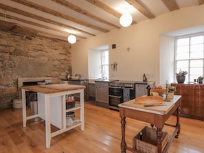 A spacious kitchen with wooden beams, a stone wall, and modern appliances. - Freswick Castle (Wick)
