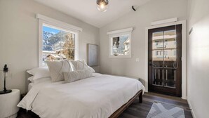 Une chambre à coucher avec un grand lit, une table de chevet, une lampe et une vue sur une montagne par la fenêtre.