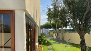 A modern building with a paved pathway leading to a door, surrounded by well-maintained greenery and a clear sky.