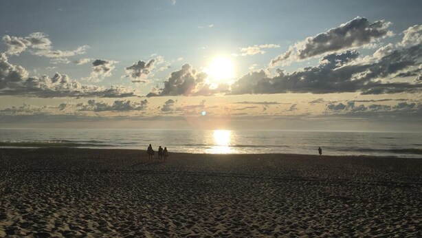 A beach with footprints leading to the water, a sunset, and a few people walking.