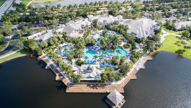 An aerial view of a resort with a central swimming pool, surrounded by palm trees and connected to the mainland by wooden walkways. - Beautiful Detached Home in Fiddlers Creek on the Golf Course (Naples)