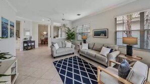 A spacious living room with two sofas, a coffee table, and a rug. There is a dining area in the background with a table and chairs. - Beautiful Detached Home in Fiddlers Creek on the Golf Course (Naples)
