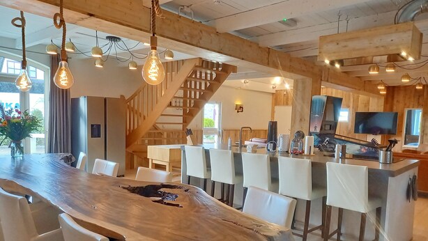 A modern dining area with a large wooden table, white chairs, and hanging light fixtures. - Pura Vida Panorama : Enjoy life ! (Oud Ade)