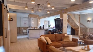 A modern living space with a wooden floor, a brown sofa, a coffee table, and a kitchen area with a bar. - Pura Vida Panorama : Enjoy life ! (Oud Ade)