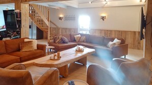 A spacious living area with a wooden staircase, a large sofa, a coffee table, and a television. - Pura Vida Panorama : Enjoy life ! (Oud Ade)