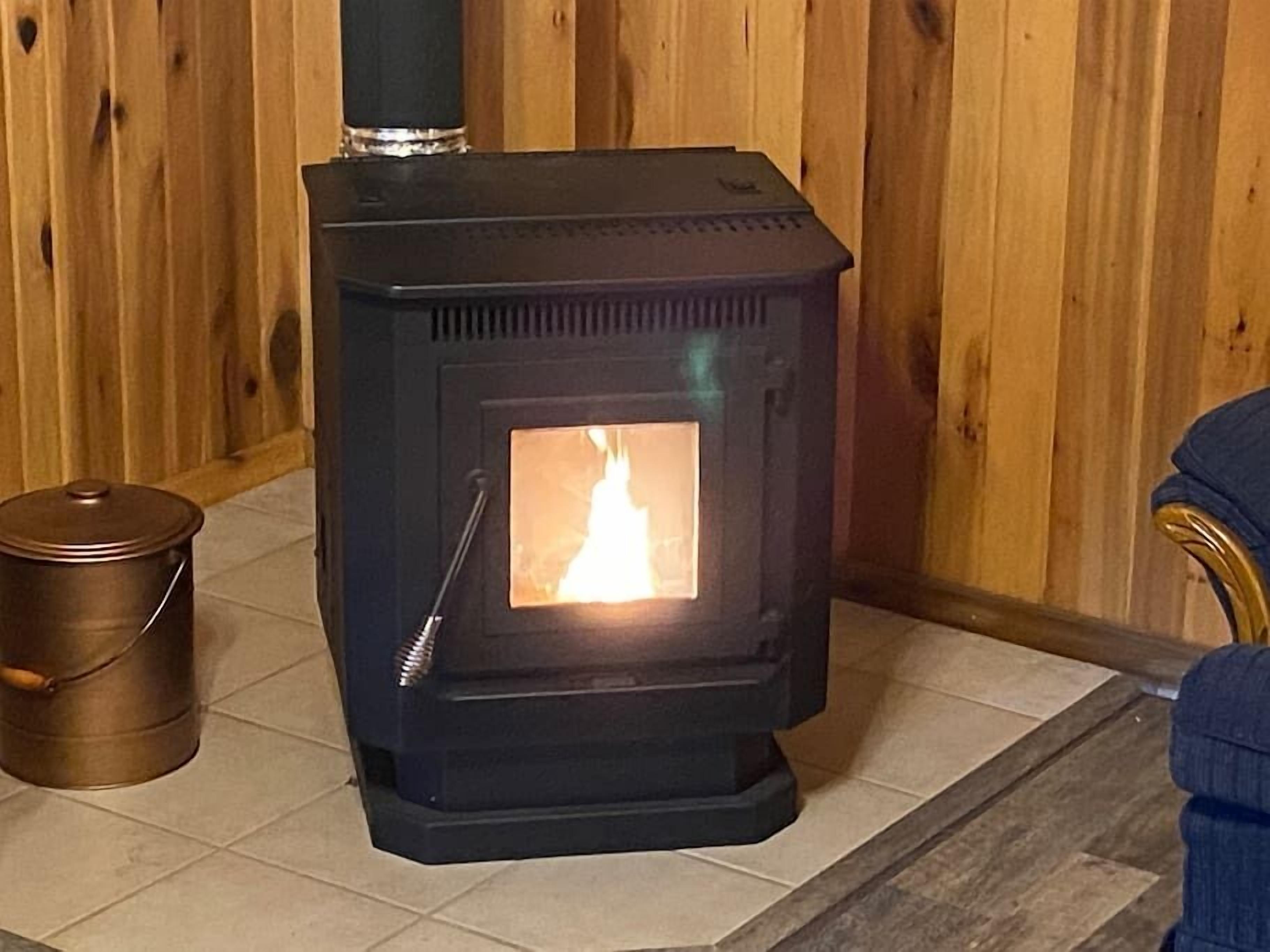 A wood-burning stove with a visible fire, a metal container, and a wooden wall.