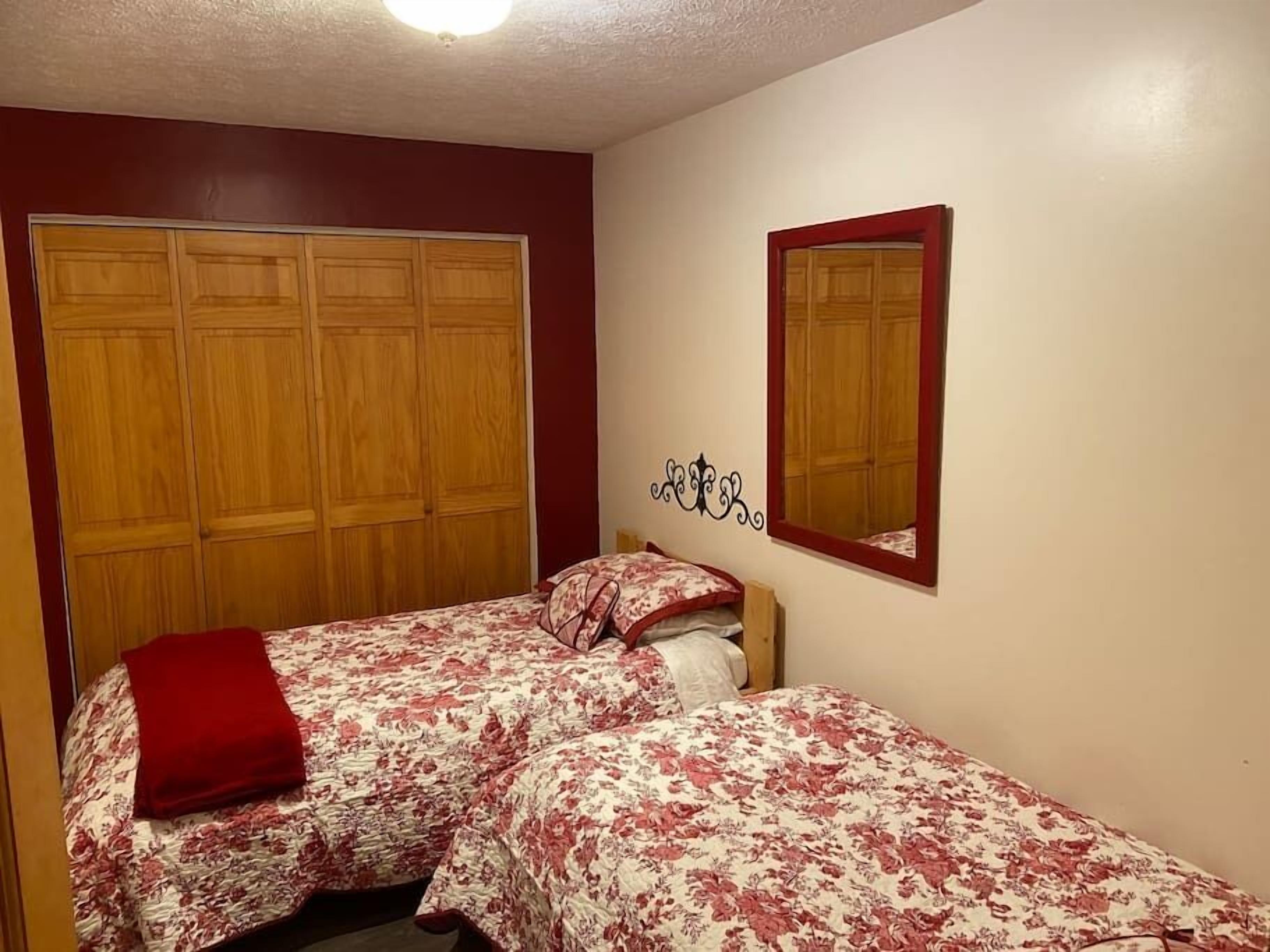 A bedroom with two beds, a wooden wardrobe, and a mirror on the wall.