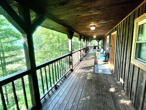 A covered wooden deck with a railing, leading to a building with windows. - "Getaway" to this private beautiful chalet. (Sneedville)