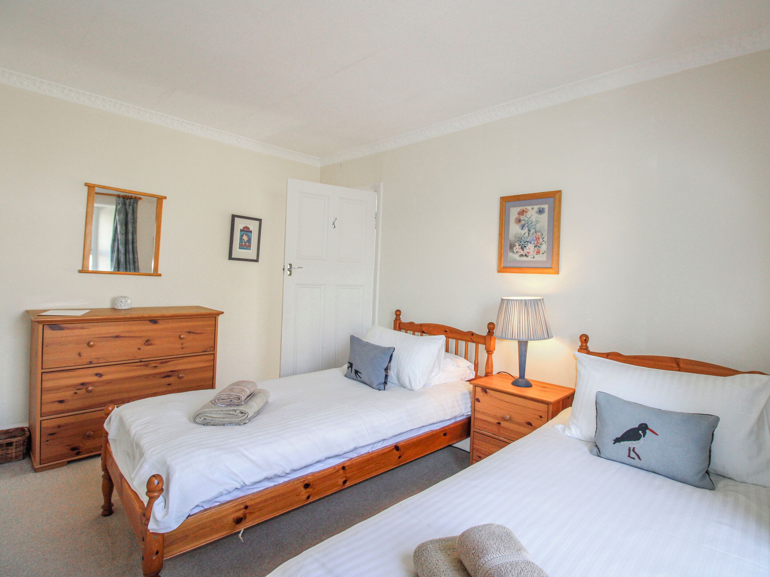 A bedroom with two single beds, a wooden dresser, a nightstand with a lamp, and a door with a keyhole.