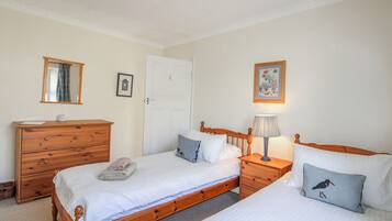 A bedroom with two single beds, a wooden dresser, a nightstand with a lamp, and a door with a keyhole.