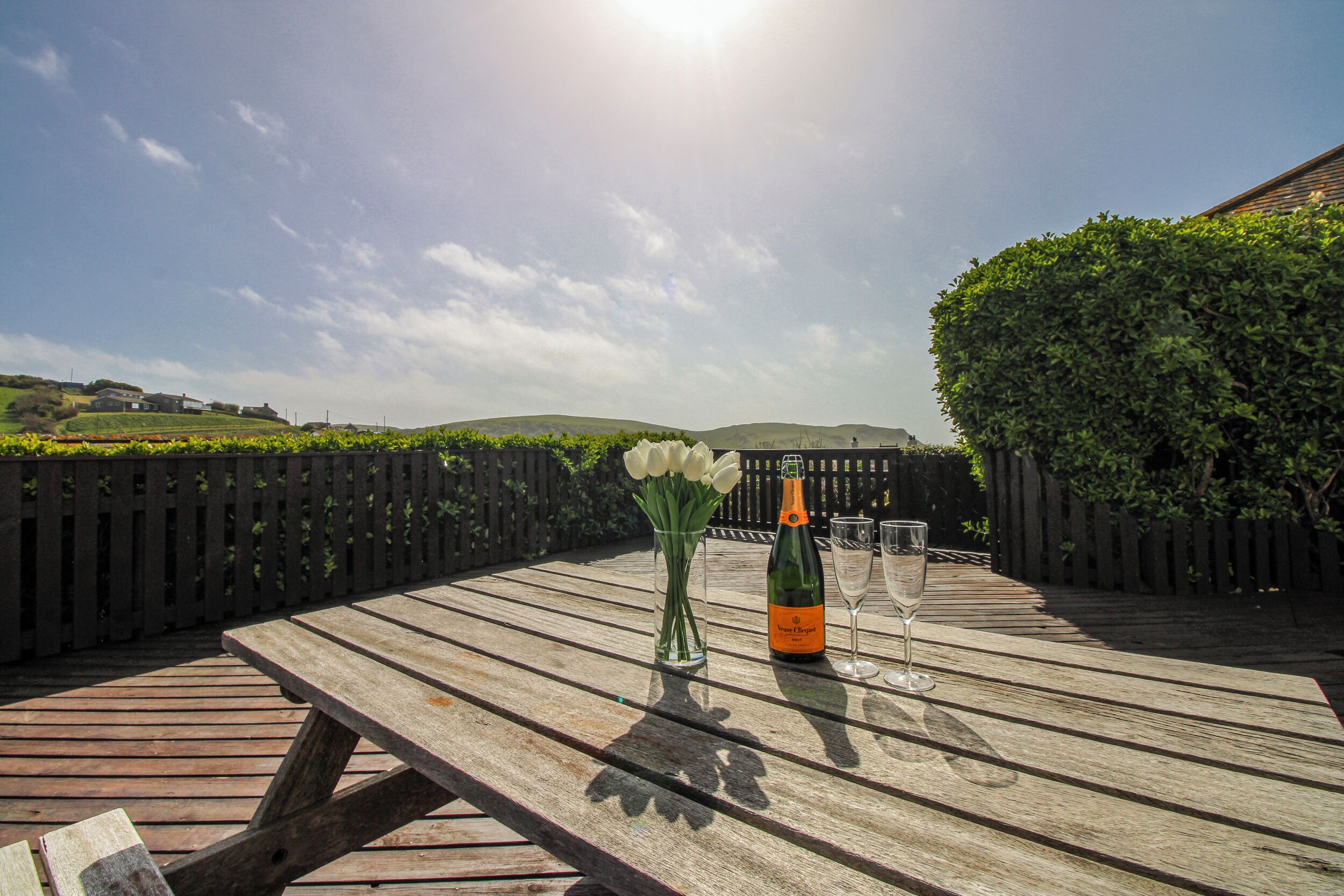 Ein Holztisch mit einer Champagnerflasche, einem Glas und einer Vase mit weißen Blumen.