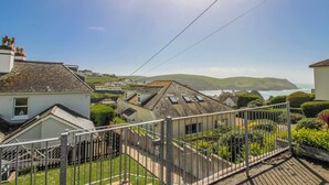 A coastal residential area with houses, a fenced garden, and a view of the sea and hills in the background. - Eddystone (Kingsbridge)