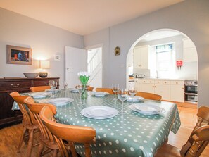 Ein Esszimmer mit einem für vier Personen gedeckten Tisch, einer Blumenvase und Blick in die Küche durch einen Durchgang.