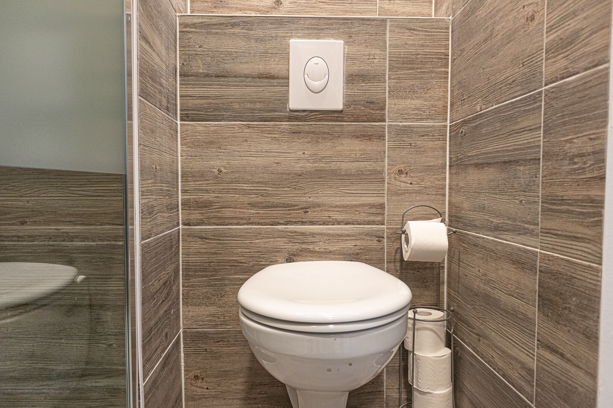 A modern bathroom with a wooden wall design, a toilet, and a toilet paper holder.
