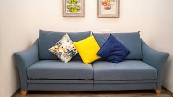 Un canapé bleu agrémenté de coussins à motifs floraux et unis, des œuvres d’art encadrées accrochées au mur et un plancher en bois.