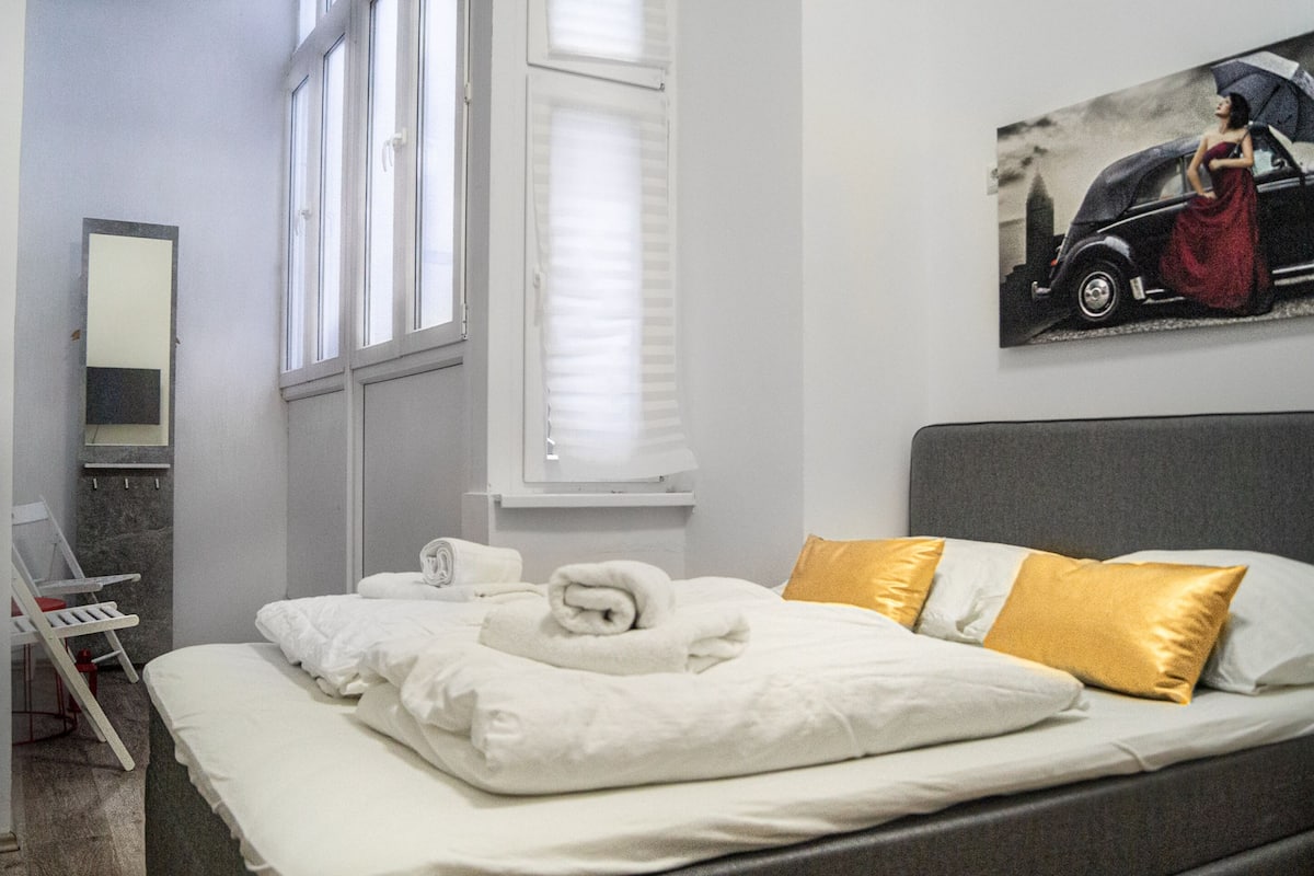 A hotel room with a bed, a chair, a window, and a painting on the wall.