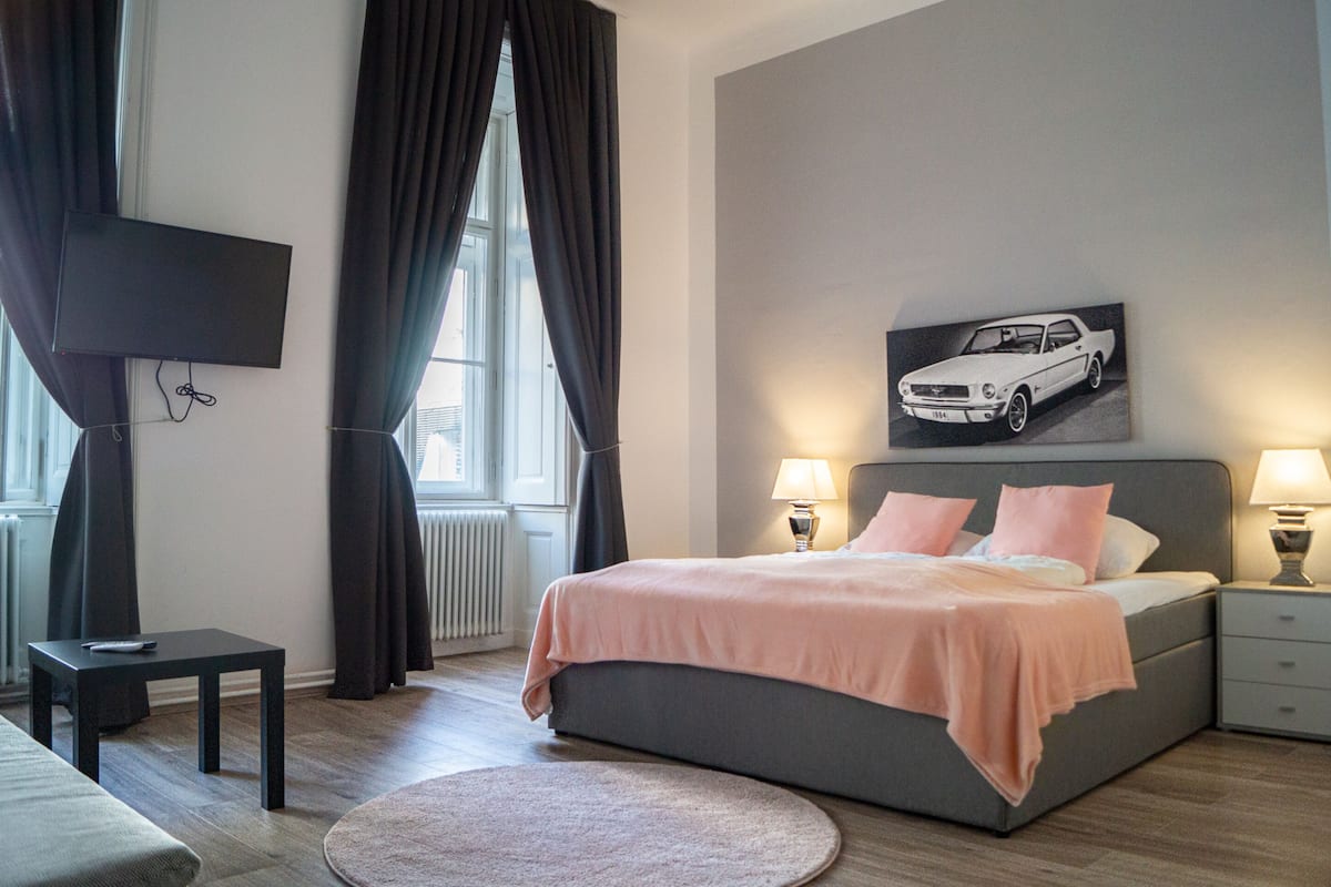A modern bedroom with a bed, bedside tables, a TV, and a car poster on the wall.