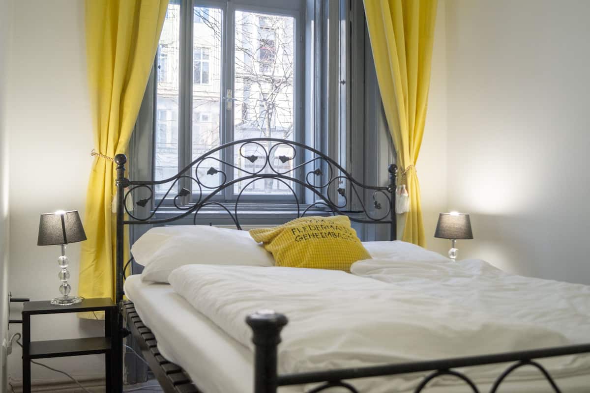 A bed with a metal frame, white bedding, and a yellow pillow. There are two bedside lamps on either side of the bed.
