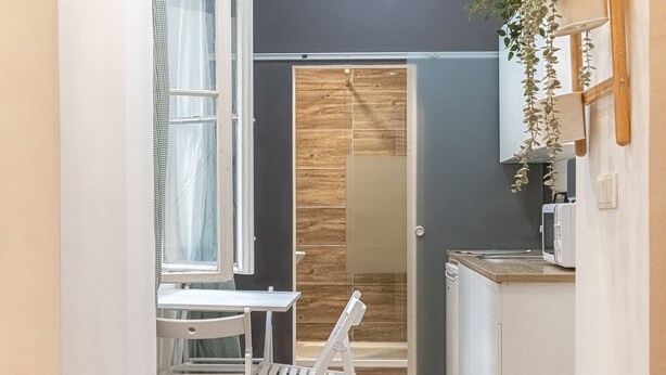 Una cocina compacta con puerta de madera, una mesa blanca con sillas y un microondas en la encimera.
