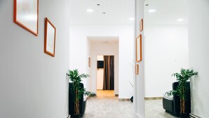 Un pasillo moderno con cuadros enmarcados en las paredes, plantas en macetas y vistas a una habitación con cama y cortinas.