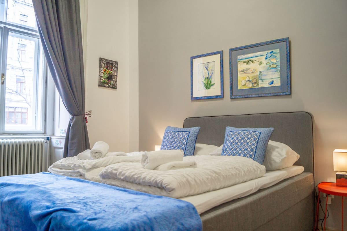 A neatly made bed with blue and white bedding, a grey headboard, and two framed pictures on the wall.