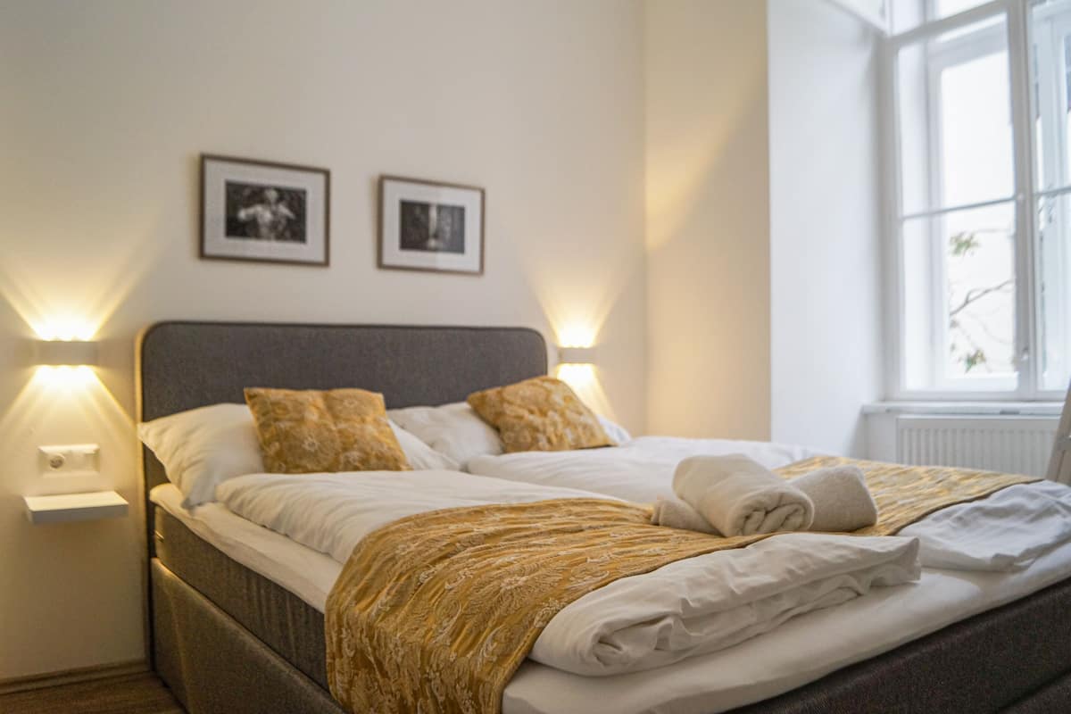 A neatly made bed with a patterned blanket, two framed pictures on the wall, and bedside lamps.