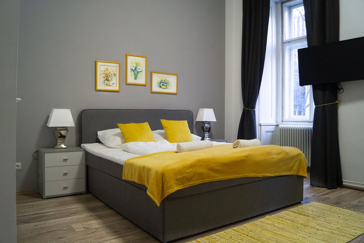 A bedroom with a bed, two bedside tables, a window with curtains, and wall-mounted artwork.