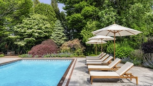 Une piscine entourée d’une végétation luxuriante, avec des chaises longues et des parasols.