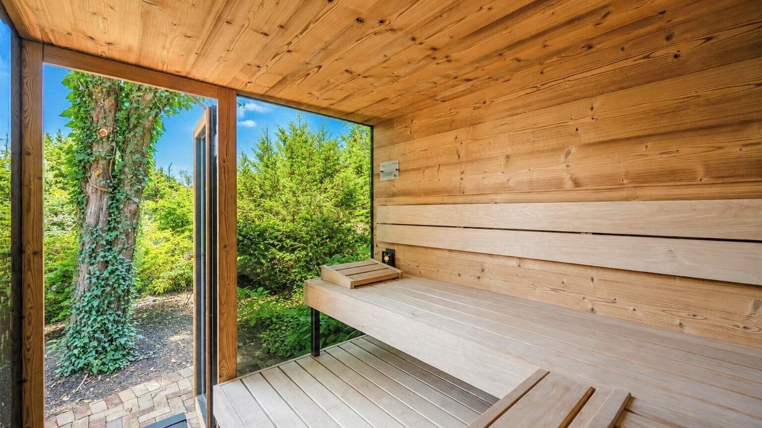 A wooden sauna with a bench and a glass door leading to a forested area.