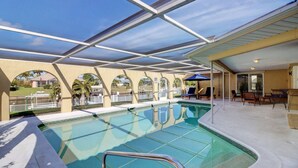 A covered swimming pool with a view of a residential area, including a house and palm trees. - 1209 SE 32nd Ter (Cape Coral)