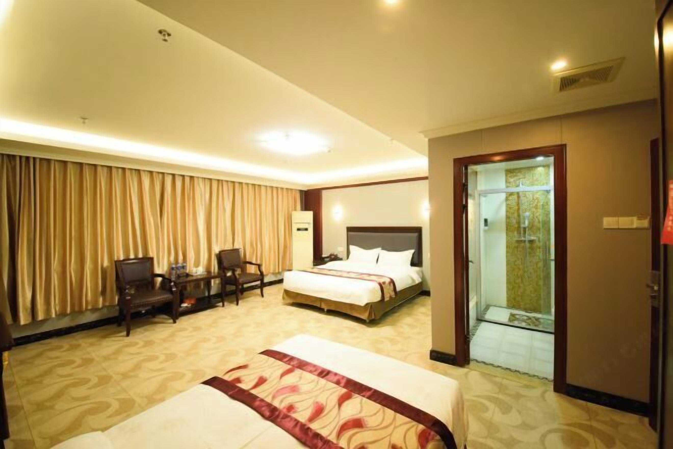 A hotel room with a large bed, a desk with a chair, a small table, and a glass-enclosed shower area.