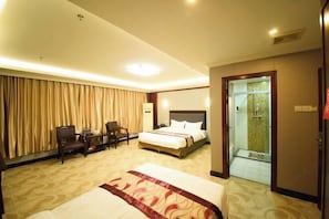A hotel room with a large bed, a desk with a chair, a small table, and a glass-enclosed shower area. - Jinhuang Hotel (Zhuhai)