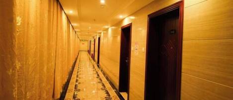 A long, narrow hallway with a patterned floor, doors on both sides, and a light-colored wall.