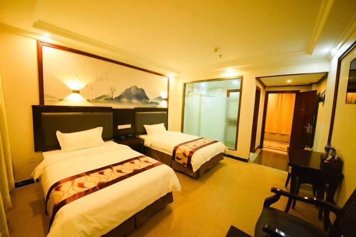 A hotel room with two beds, a large mirror, a desk, and a view of the outside.