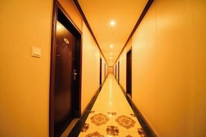 Een hotelgang met een lange, smalle gang, deuren aan beide zijden en een vloer met een patroon.