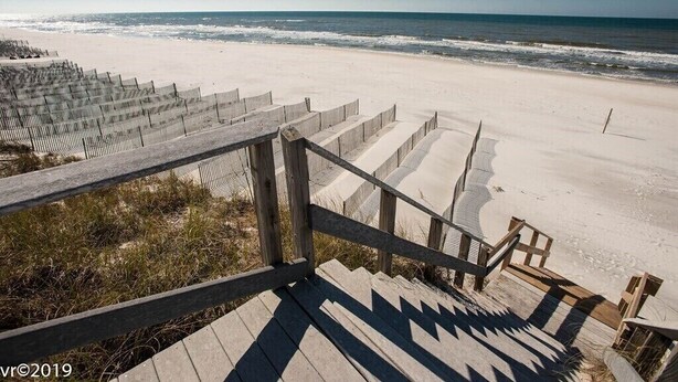 Una escalera de madera que baja hacia una playa de arena con vistas al océano.