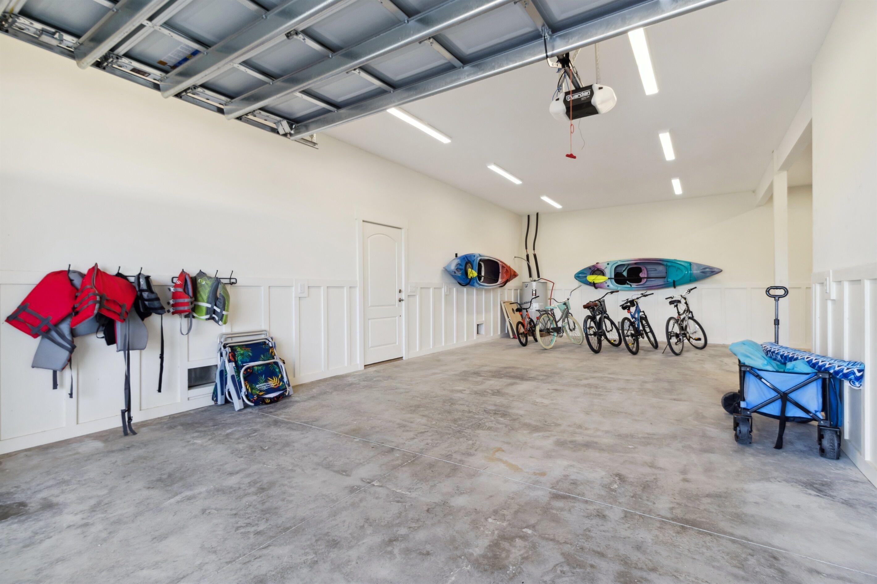 Amplio espacio interior con suelo de concreto, paredes blancas y techo metálico. Se observan varios kayaks y bicicletas, además de un cochecito azul.
