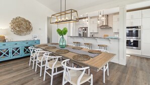 Una cocina moderna con armarios blancos, electrodomésticos de acero inoxidable y una mesa de comedor de madera con sillas blancas.
