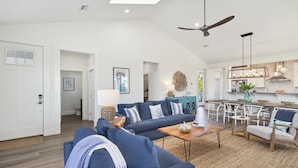 A spacious living room with a large sofa, a coffee table, and a dining area with chairs and a table. - Salt Therapy – Stylish New 4BR Home, 5 stars (Cape San Blas)