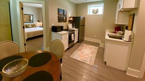 Una cocina compacta con zona de comedor, un refrigerador pequeño y un microondas. Hay una alfombra en el suelo y una ventana que proporciona luz natural.