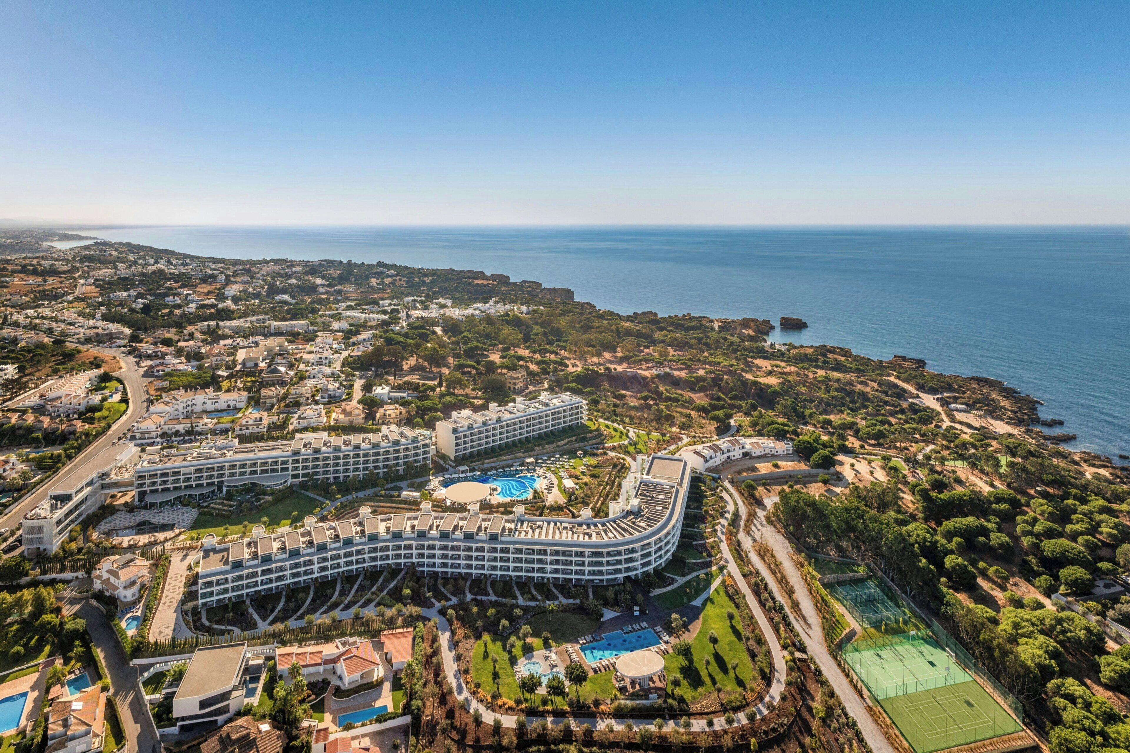 Ein großes Resort mit mehreren Gebäuden, einem Schwimmbad, Tennisplätzen und Meerblick.