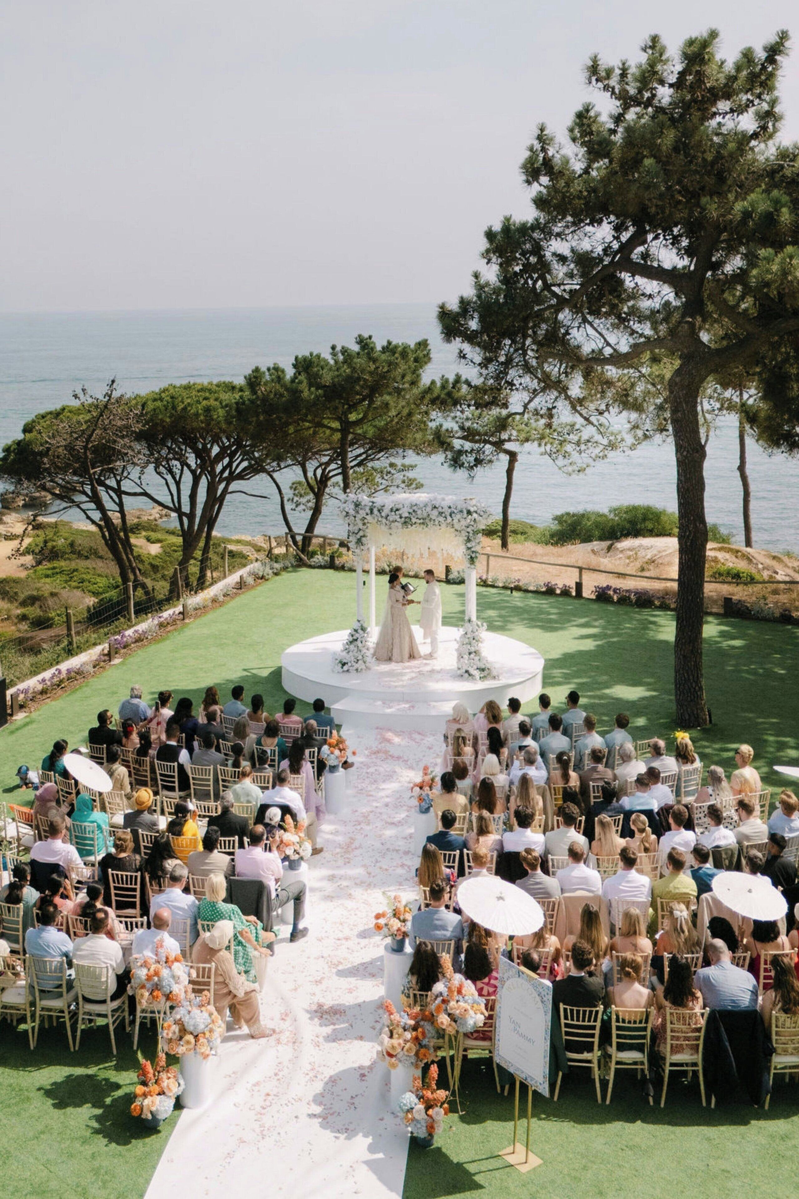 Ceremonia de boda al aire libre con invitados sentados en sillas frente a un escenario con un arco floral.