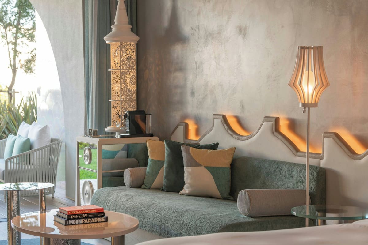 A modern living room with a sofa, a coffee table, and a lamp. There is a bookshelf with books and a decorative item on the sofa.