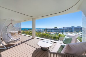 Enjoy the serene view from this outdoor balcony with a hanging chair, round table, and comfortable sofa.