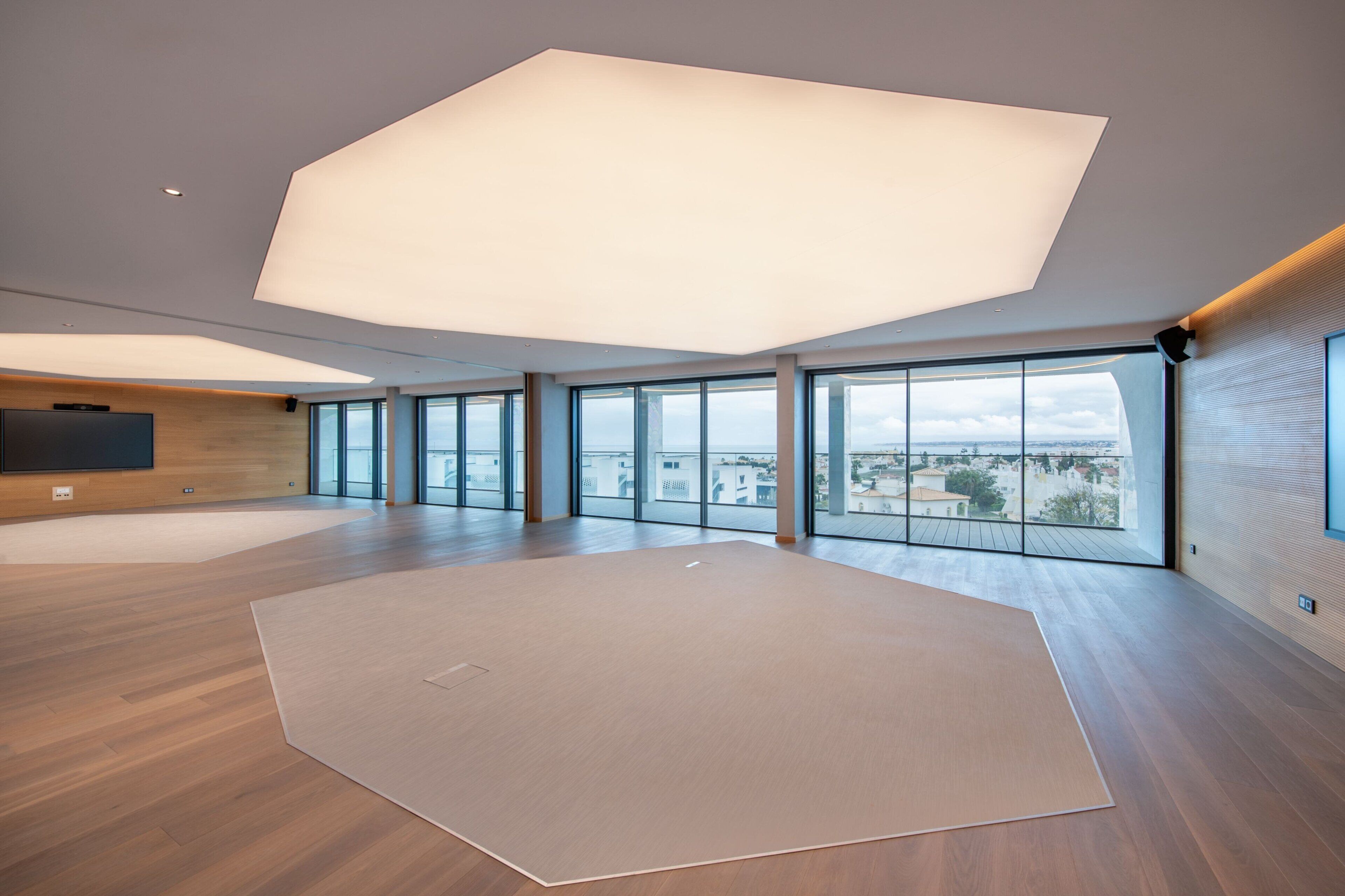Una habitación amplia con ventanas grandes, techo alto y televisor de pantalla plana montado en la pared.