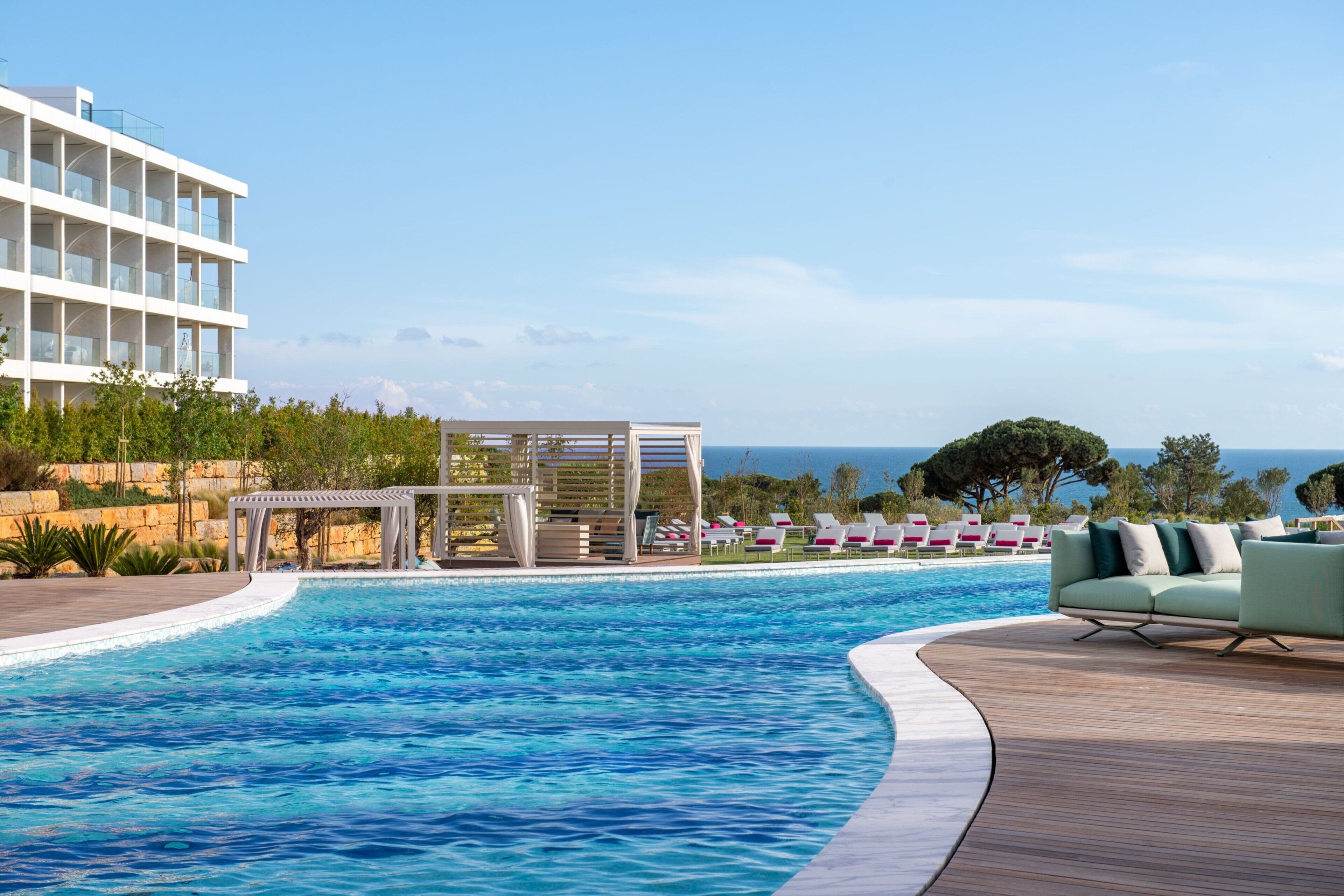 A swimming pool with a wooden deck, lounge chairs, and a building with balconies.